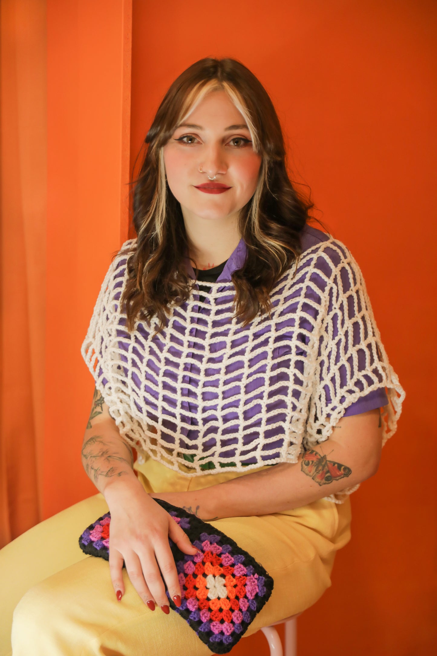 Un portrait doux et souriant cadré à l' américaine dans un univers orange des année 80 avec un croptop blanc de la série "OPEN" courte.frange ; les mains posées sur les cuisses qui tiennent une pochette granny courte.frange également.
Deux créations au crochet unique qui raconte la douceur, la tendresse et la nostalgie de notre enfance. 
Photographie en collaboration avec La Fripothèque (friperie :sélection de vêtements du magasin pour le shooting)