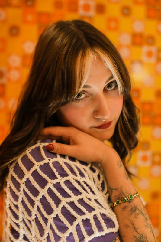 Portrait doux et attentif dans un univers orange des année 80 avec un croptop blanc de la série "OPEN" courte.frange ; une main visible posée sur son épaule qui maintient son visage.
Une création au crochet unique qui raconte la douceur, la tendresse et la nostalgie de notre enfance. 
Photographie en collaboration avec La Fripothèque (friperie :sélection de vêtements du magasin pour le shooting)